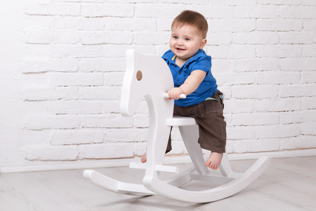 Little smiling baby sitting on a white horse, wooden rockingの写真素材