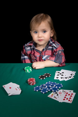Child sitting at a poker table with cards and chips with one hand leaning on his elbowの写真素材