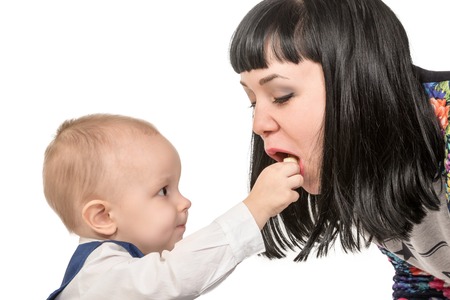 Little child puts in the open mouth of his mother food isolated on white backgroundの写真素材