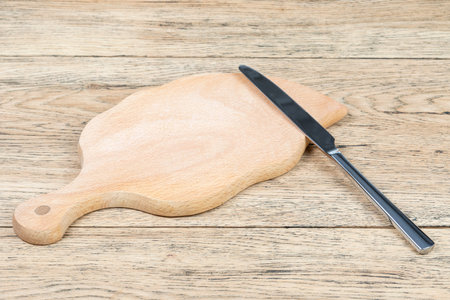 Dining knife and wooden cutting board in the shape of a leaf on an old wooden tableの写真素材