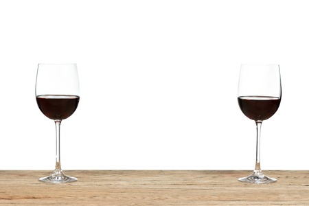 Two half-filled glass of red wine standing on the edge of a wooden table isolated on white backgroundの写真素材