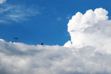 Four skydivers with open parachutes floating in the blue sky with cloudsの写真素材