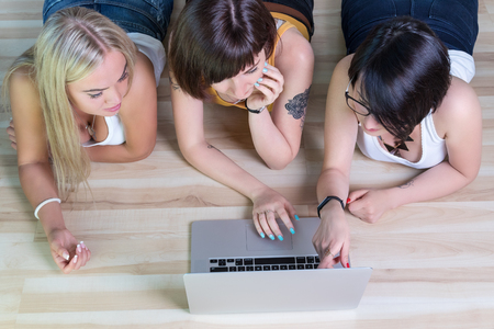 Three women lying on the floor point to the laptop screen, view from aboveの写真素材