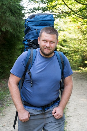 Close-up portrait of a bearded traveler with a backpack on his back on the forest backgroundの写真素材