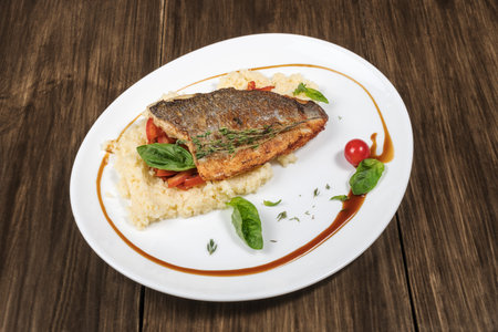 Fried fish dorado with couscous, decorated with cherry tomatoes and salad leaves