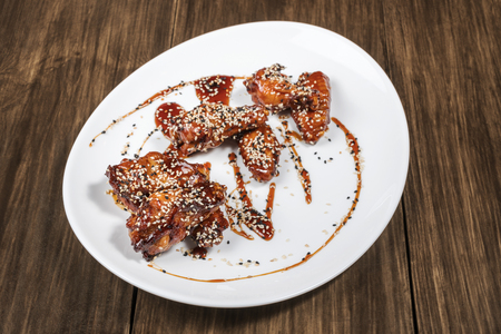 Grilled chicken wings and legs with sauce, served on a white plate on old wooden tableの写真素材