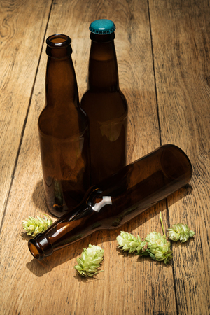 Three brown bottles of beer next to the green branches of hops. One full closed, two empty and openの写真素材