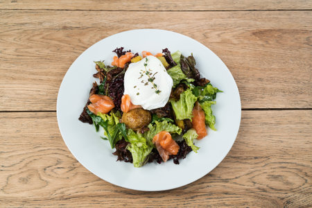 Delicious salad with salmon, baked potatoes, lettuce and mushrooms served on a white plate on old wooden tableの写真素材