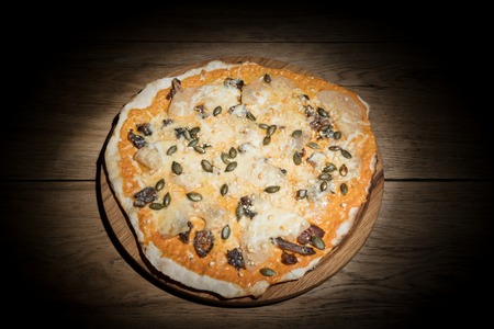 Sweet pizza with pineapple, dried pears and pumpkin seeds, served on a wooden plate in the darkの写真素材