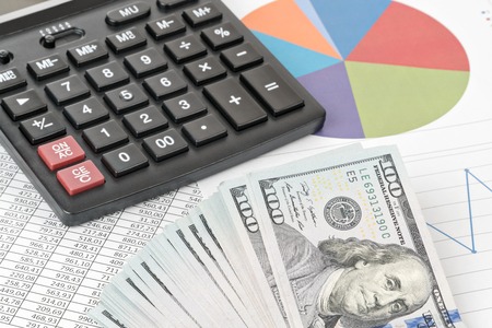 Business still-life. Calculator and a pack hundred dollar bills lying on the graphs and tables with numbersの写真素材