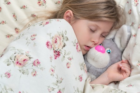 Little cute girl sleeping under a blanket with a plush toy rabbit, closeupの写真素材