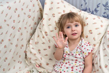 Portrait of a cute baby girl sitting in the bed, and put forward open palm