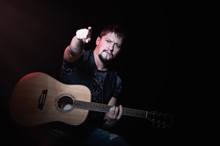 Bearded guitarist with an acoustic guitar in concert indicates the index finger on viewersの写真素材