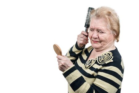 Old woman brushing her hair in front of a small wooden mirror isolated on white backgroundの写真素材