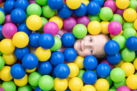 Child hid in colorful balls so that one head sticks outの写真素材