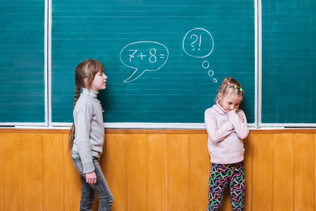 One girl, standing at the school board, assigns a mathematical task to another girl who can not solve itの写真素材