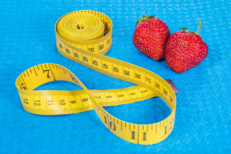 Ripe strawberry with yellow metric tape measure on a blue sports carpetの写真素材