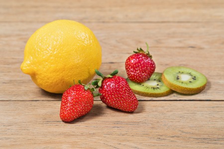 Large whole lemon, ripe strawberry and kiwi slices on an old wooden tableの写真素材
