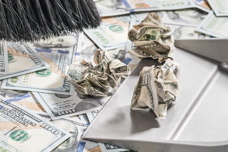 Broom sweeps crumpled dollars in the scoop from the surface covered with new dollars, close-upの写真素材