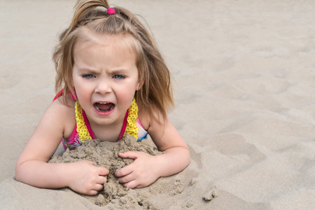 Little girl lying on the sand on the beach screaming mouth wide open, close-upの写真素材