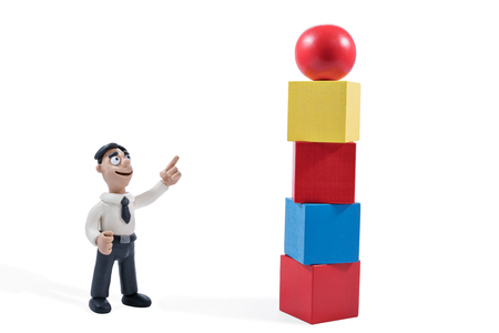 Plasticine businessman points to a toy tower from wooden blocks with the ball at the top isolated on white backgroundの写真素材