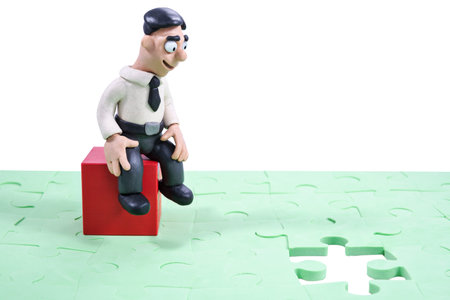 Plasticine businessman sitting on wooden blocks and looks at a hole in the stacked puzzle isolated...