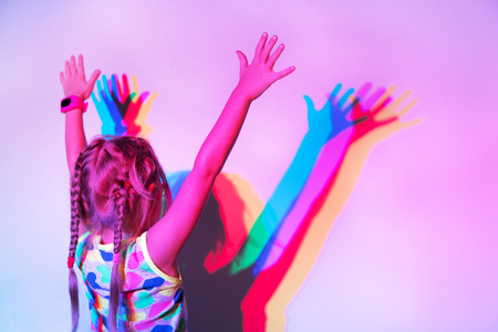 Girl stands at the wall with her hands up, on which her silhouette is reflected in different colors. Back viewの写真素材