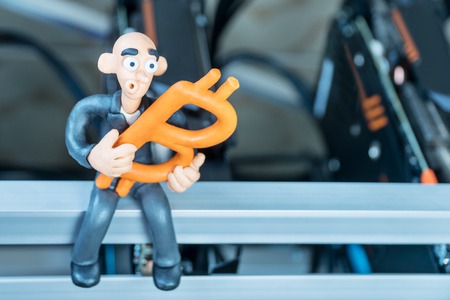 Bald plasticine businessman sits on a mining farm with bitcoin in his handの写真素材