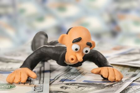 Surprised bald plasticine businessman lies on a pile of hundred dollar billsの写真素材