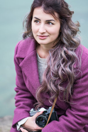 Portrait of a beautiful woman in a coat with a camera in hands