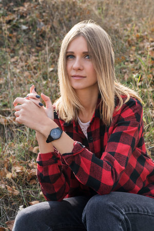 Portrait of a beautiful blonde woman in a shirt in a cage sitting on the grass