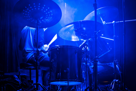 Drummer plays the drums at a concert with blue lighting in the smokeの写真素材