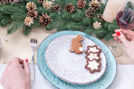 Female's hands holding a glass of wine at the Christmas table with cookies in a plate