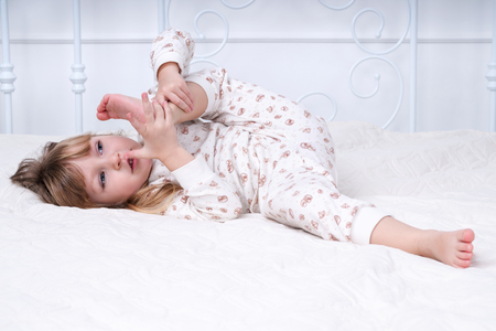 Child does gymnastics lying on a bed, having lifted a leg to a headの写真素材