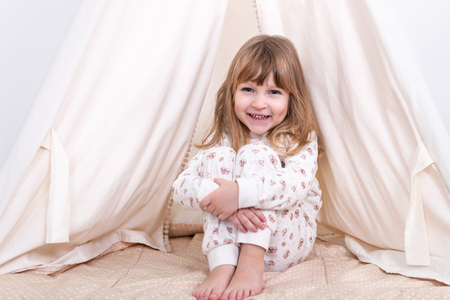 Portrait of a little smiling girl sitting on the floor near the tent and hugging her kneesの写真素材
