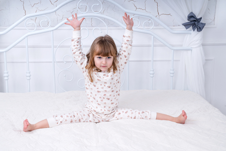 Little beautiful girl in pajama doing stretching sitting in bed in the morningの写真素材