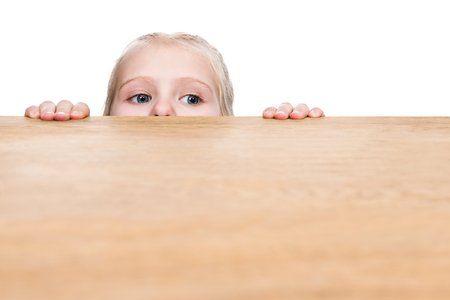 Child sticks his eyes out from under the table and looks sideways, isolated on a white backgroundの写真素材