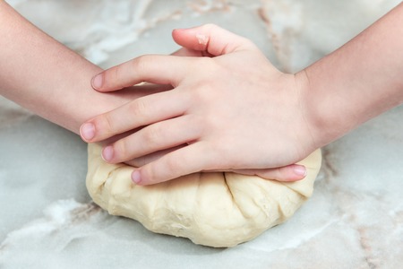 Children hands knead the dough on the table, closeupの写真素材