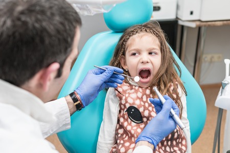 Dentist prepared to drill a tooth for a little girl sitting in a dental chair with her mouth openの写真素材
