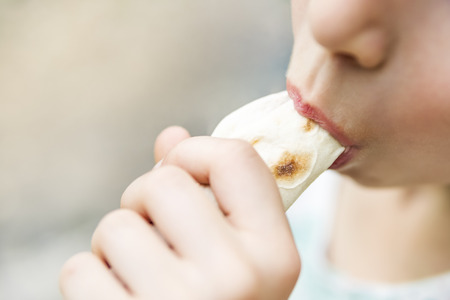 Hands hold shawarma, which bites the mouth, close-up, blurred backgroundの写真素材