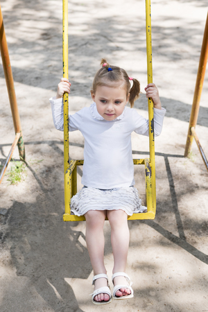 Little beautiful serious girl riding on a dilapidated metal swingの写真素材
