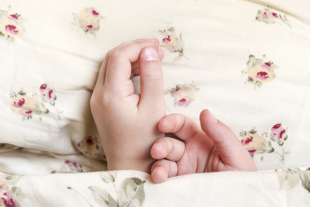 Two children hands peeping out from under the blankets, close-upの写真素材