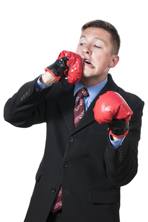 Businessman in red boxing gloves beats himself in the face, isolated on white backgroundの写真素材