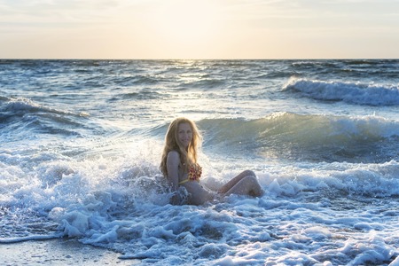 Portrait of a woman sitting in the water in the sea at sunsetの写真素材