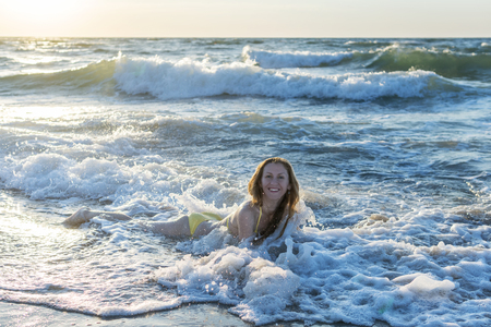 Woman lies in the surf zone in the sea waves at dawnの写真素材
