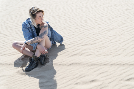 Portrait of a woman in shorts and jacket, sitting on the sand in the desertの写真素材