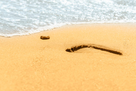 Trail of foot next to pebbles in the sand near the line of the sea