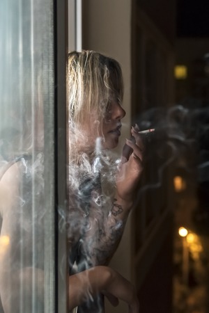 Smoking woman with a tattoo in the window at nightの写真素材