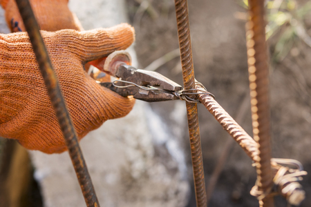 Hands of the builder in orange gloves, twisting the armature with wire using pliersの写真素材