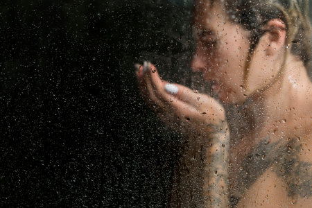 Beautiful woman in the shower washing her face, against a dark background
